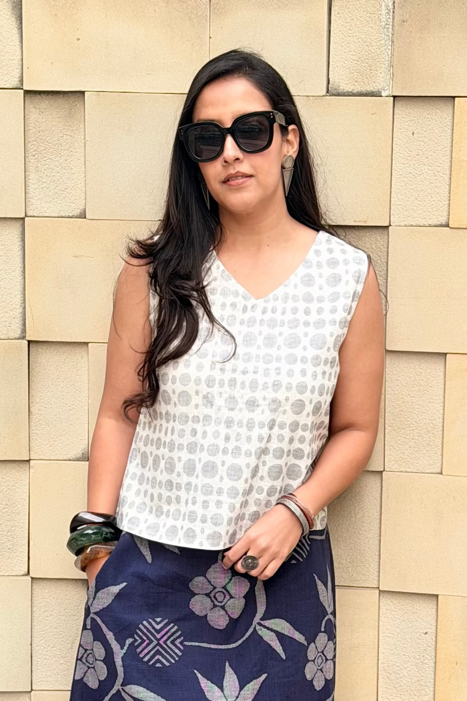 Woman wearing a white top and blue floral skirt against a stone wall.